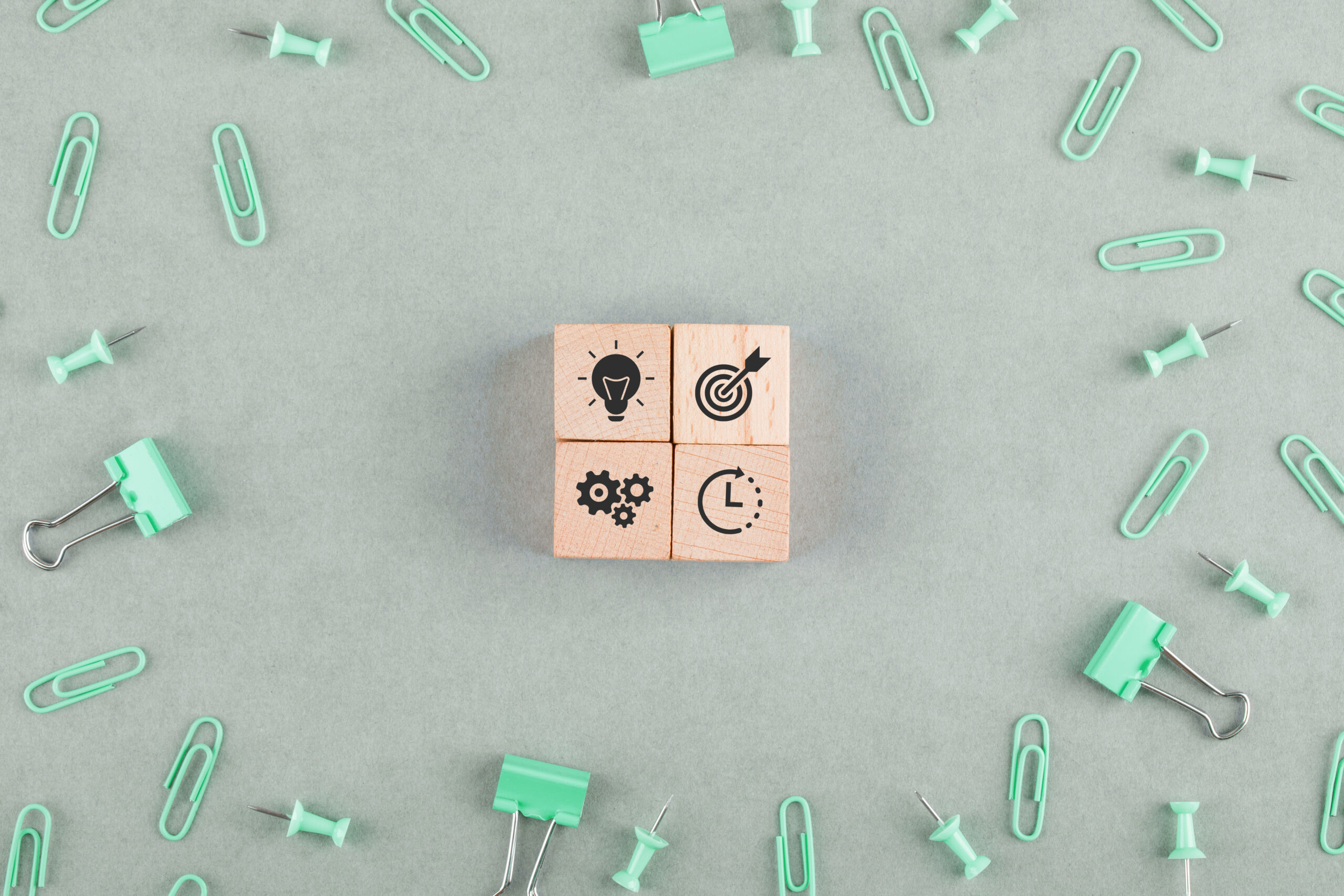 Business office concept with wooden blocks with icons, paperclips, binder clips on sage color background top view. horizontal image